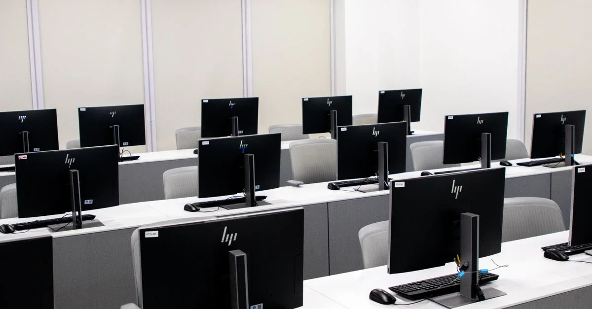 Salle informatique spacieuse et minimaliste avec des rangées d'écrans noirs et du mobilier élégant.